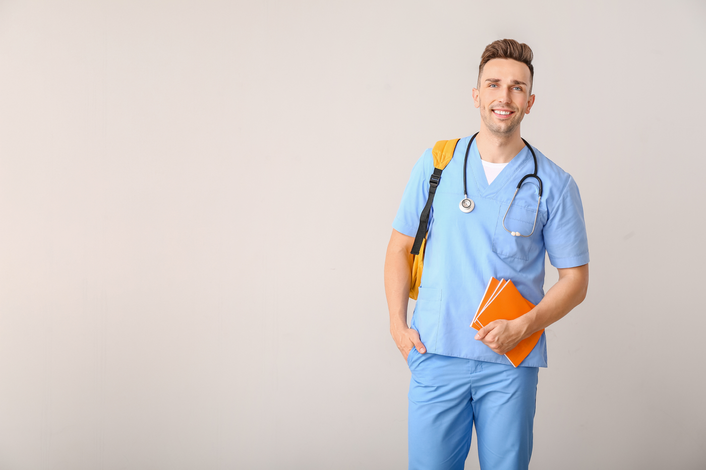 Nurse holds notebooks with backpack over his shoulder and stethoscope around neck